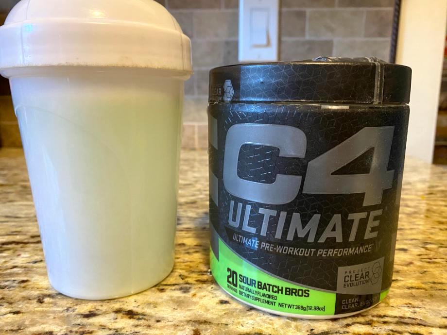 A shaker cup is next to a well-posed can of C4 Ultimate Pre-Workout  with the front label displayed prominently