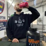A man is shown throwing back a shake made with Rival Nutrition Mass Gainer.