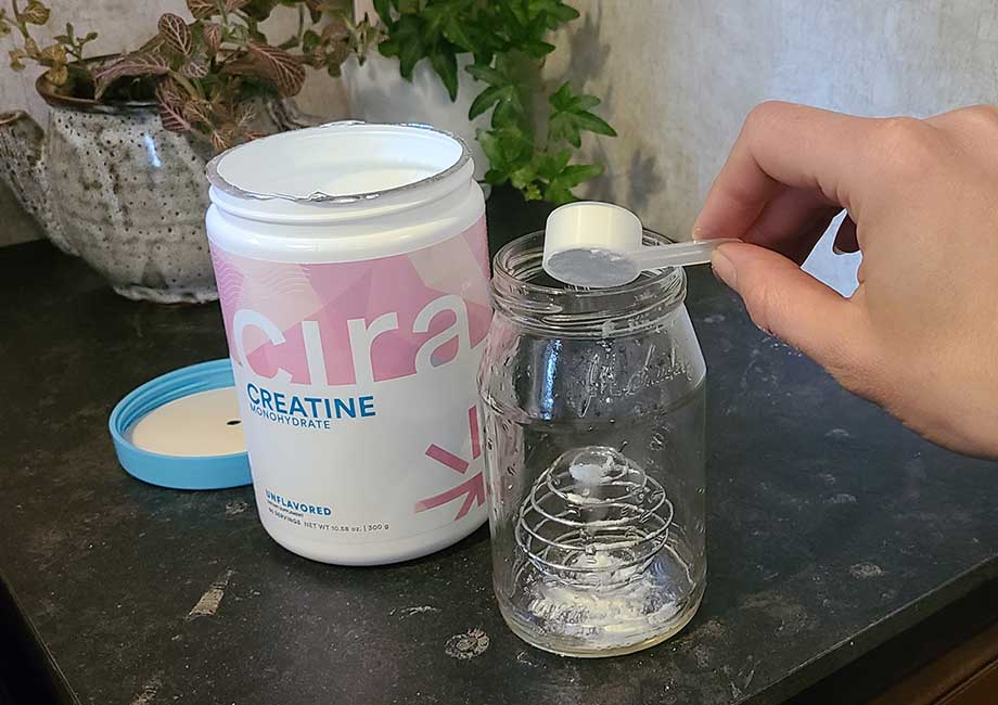 Someone scooping Cira creatine into a jar with a shaker ball