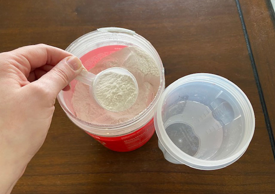 Looking down on a scoop of Clear Naked Whey protein as it's being scooped out of the container.