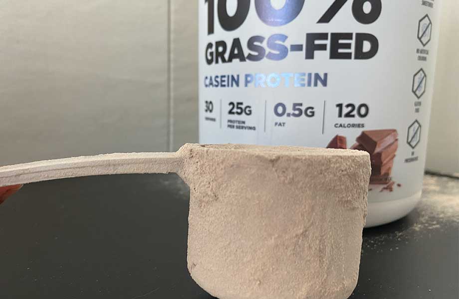 Really close up, looking at the side of a scoop of Transparent Labs Casein Protein powder. The words '100% Grass-Fed" can be seen in the background.