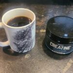 A mug of coffee and a container of creatine sitting on a counter next to each other