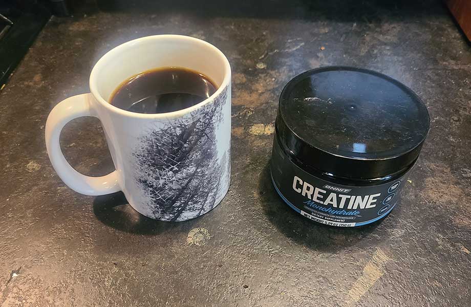 A mug of coffee and a container of creatine sitting on a counter next to each other
