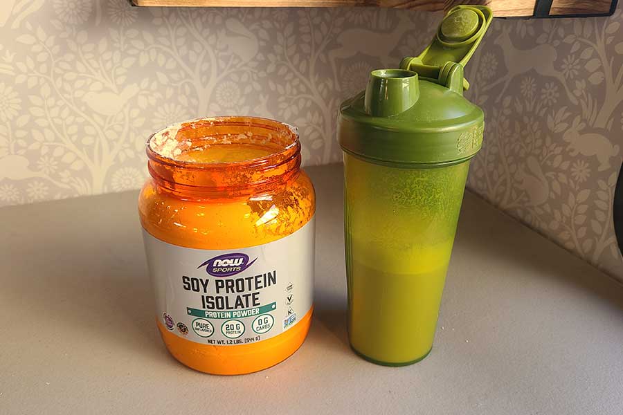 A container of Now soy protein next to a shaker bottle