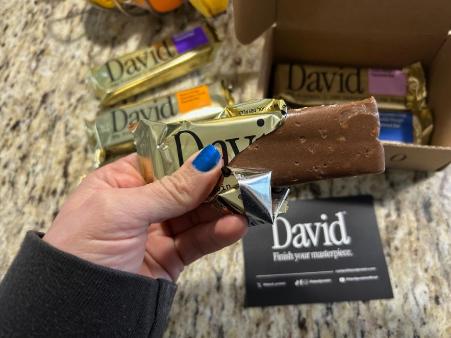 A hand holding an opened David Protein Bar