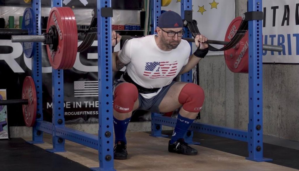 man squatting using a barbell and power rack