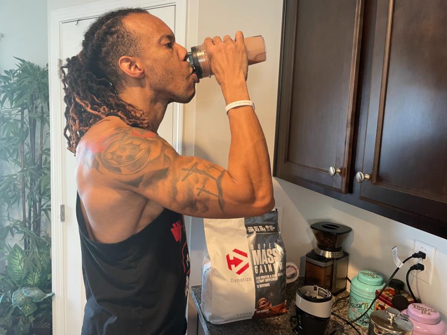 A person drinks a shake made from Dymatize Super Mass Gainer.