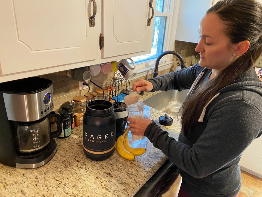 Woman dumping Kaged Clean Meal scoop into a blender cup