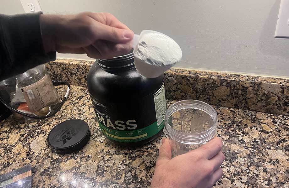 A person dumps a huge scoop of Optimum Nutrition Serious Mass into a shaker cup