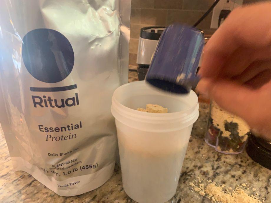 A hand dumps Ritual Protein Powder into a cup
