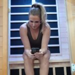 A woman uses her phone while sitting in a Dynamic Infrared Sauna