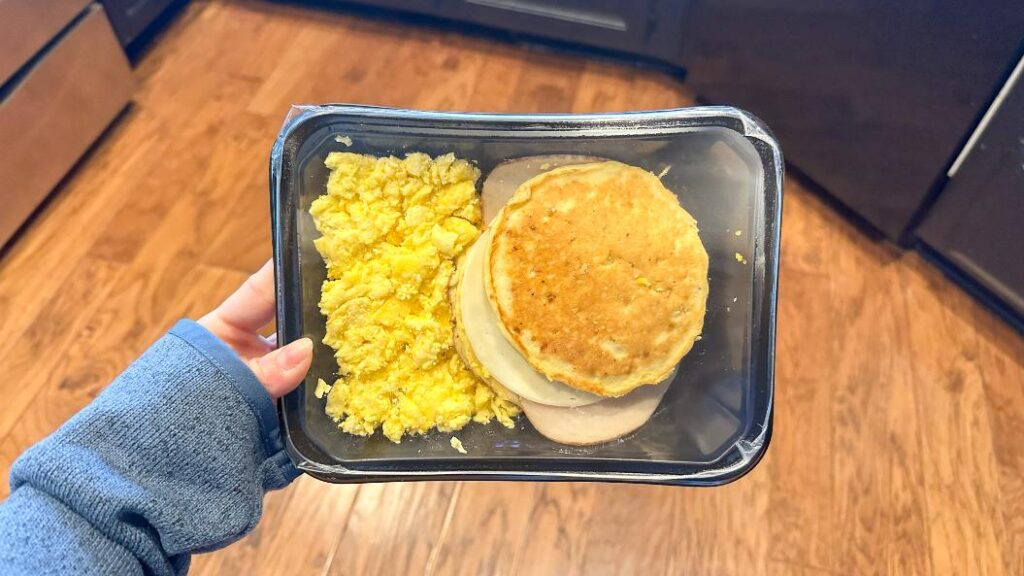 Person holding a prepared meal from Eat Clean of Pancakes and scrambled eggs