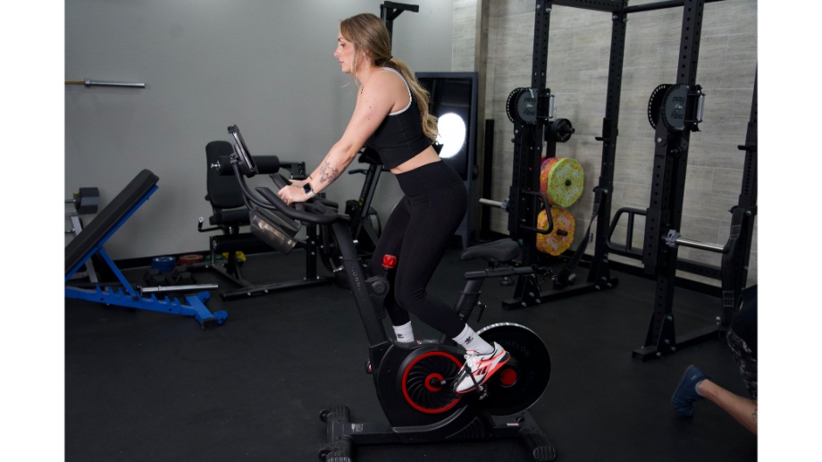 Woman standing up riding the echelon ex5 bike with other gym equipment in the background