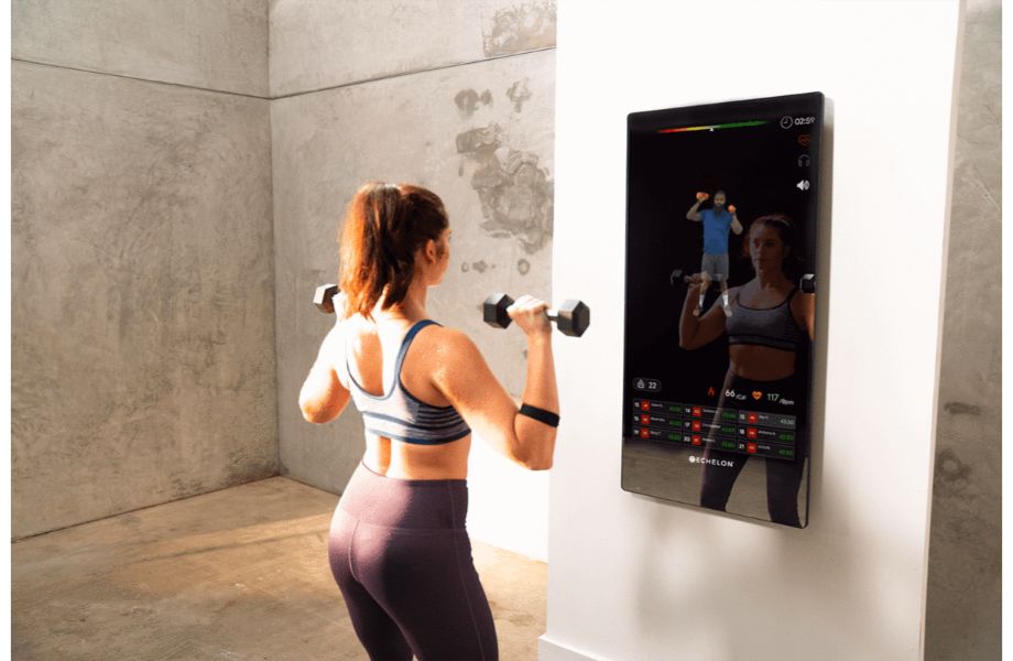 Product image of the Echelon Reflect showing a woman working out with dumbbells in front of the reflective screen.