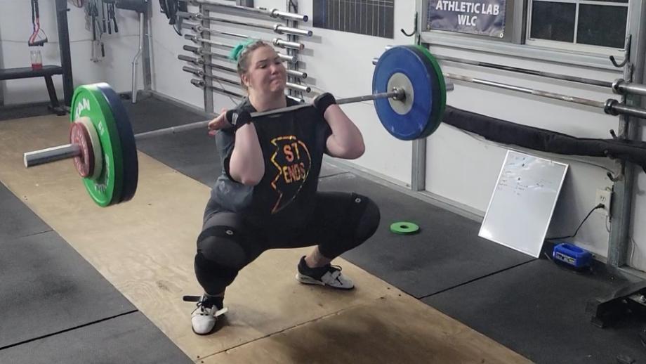 A woman performs a barbell clean with the Eleiko IWF Training Bar.