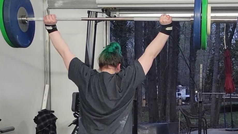 A woman holds the Eleiko IWF Weightlifting Training Bar overhead with a hefty load.