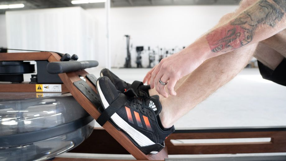 a man strapping into foot cradles on a rowing machine