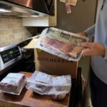 A person holds up a package of free bacon from ButcherBox.