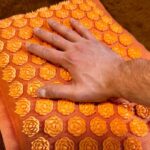 A hand feels the texture of a Pranamat Accupressure Mat.