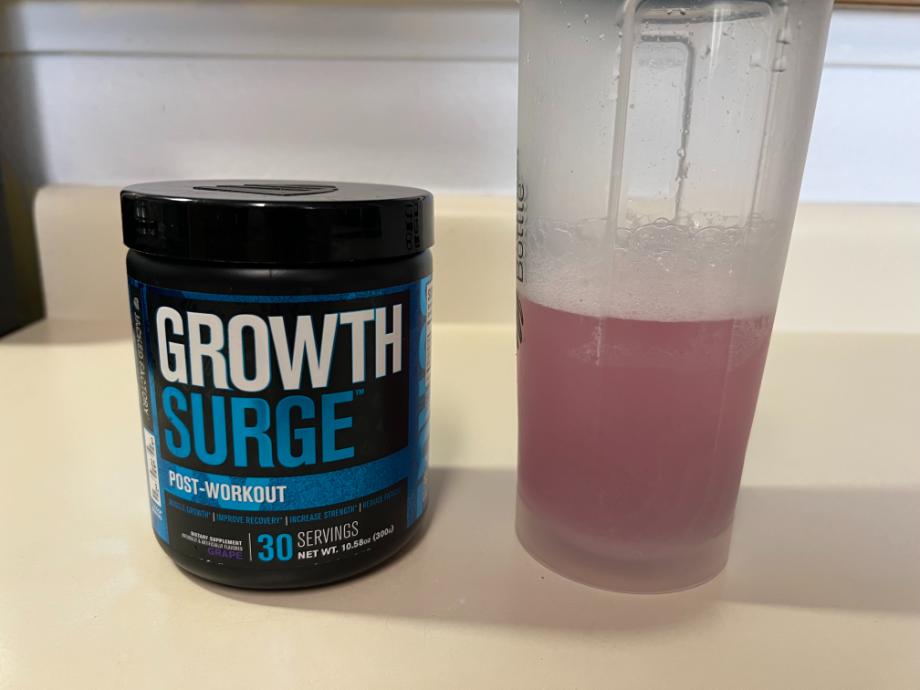 A freshly mixed shaker cup of Jacked Factory Growth Surge rests next to the container.