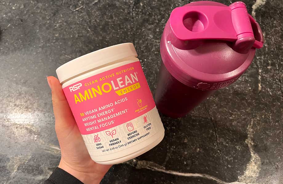 A container of AminoLean Pre-Workout is held next to a shaker bottle with the front label on display