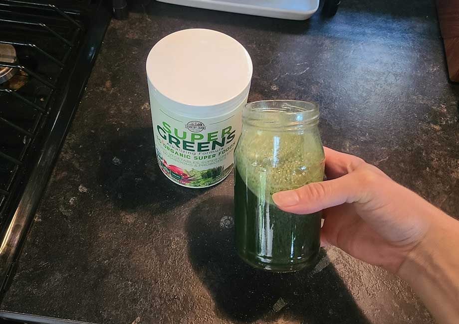 An image of a woman holding a glass of Country Farms Super Greens