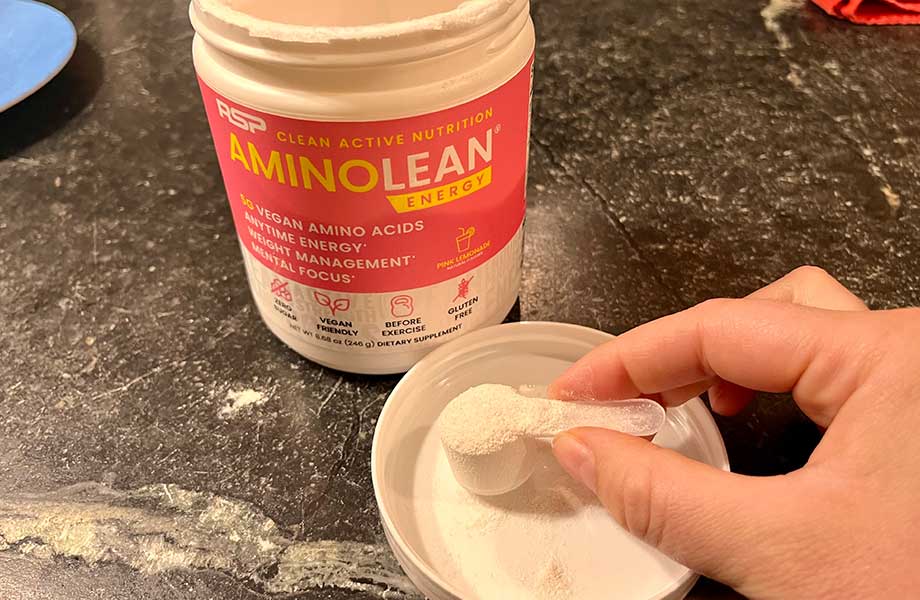 A hand holds a scoop of AminoLean Pre-Workout