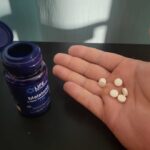 A hand holding Life Extension Melatonin tablets.