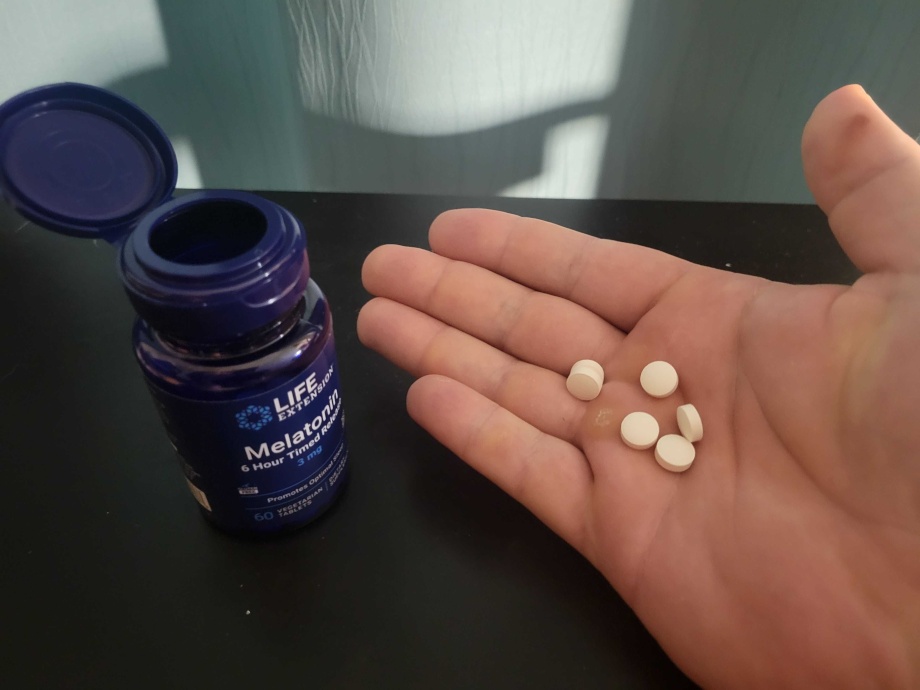 A hand holding Life Extension Melatonin tablets.