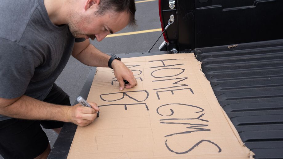 Coop using a Sharpie to write "Home gyms are better" on a piece of cardboard