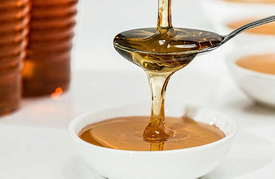 Honey pours over a spoon into a white ceramic bowl.