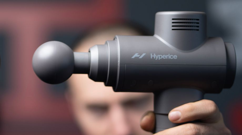 Coop's face blurred behind a closeup of the Hypervolt 2 massage gun