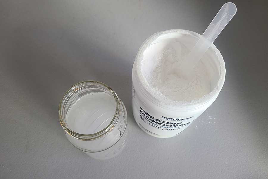 Top-down image of an open Nutricost creatine container next to a glass of mixed creatine
