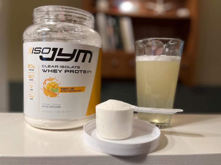 A scoop of ISO JYM 100% Whey Protein rests front and center near the container and a shake.