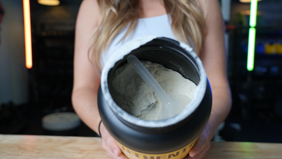 A person holds up an open container of Jacked Factory Authentic Iso Whey Protein.