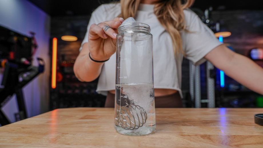 A scoop of Nitrosurge Pre-Workout is dumped into a glass bottle with a stainless steel shaker ball