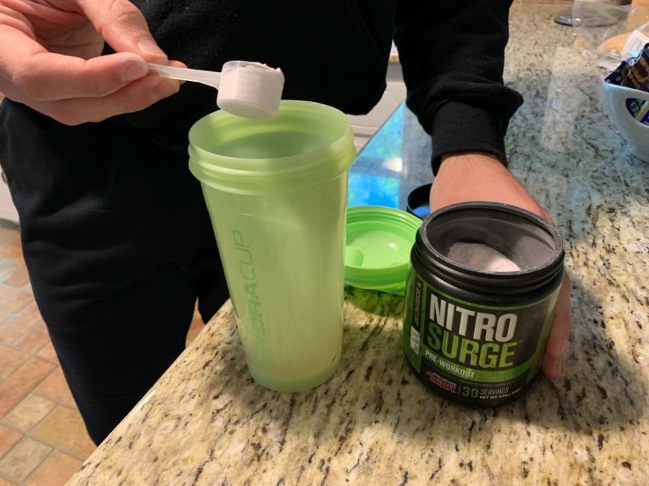 A scoop of Nitrosurge Pre-Workout being poured into a shaker cup