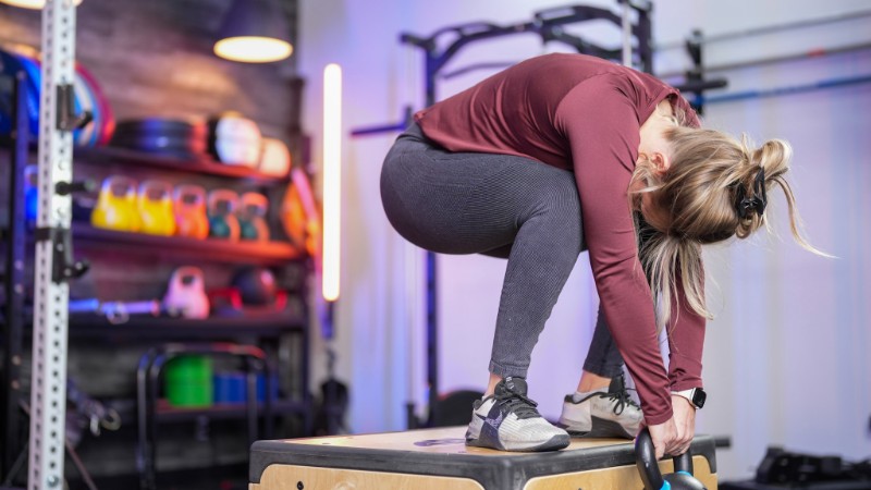 Side view of a woman performing a Jeffrson Curl, halfway through a rep