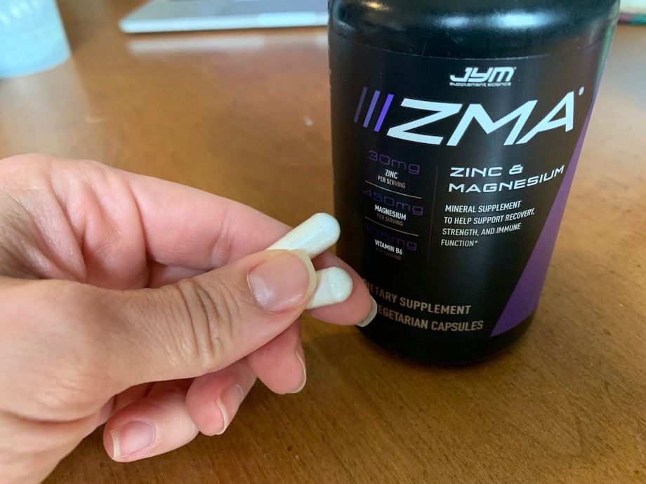 A hand holds up 2 capsules next to a bottle of Jym Zma.