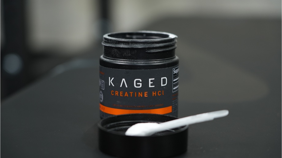 A scoop of Kaged Creatine HCl rests on the lid in front of the opened container.
