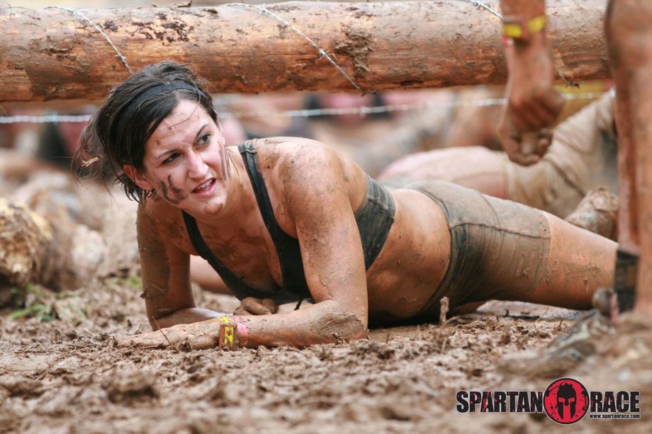 A woman army crawling through mud during an obstacle course race