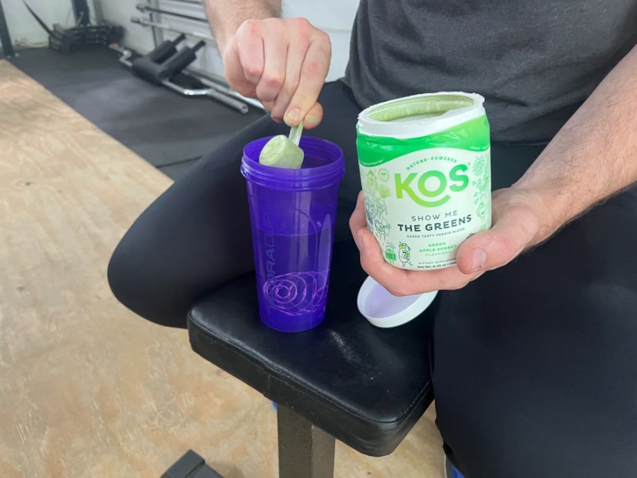 An image of a man scooping KOS Show Me the Greens into a shaker