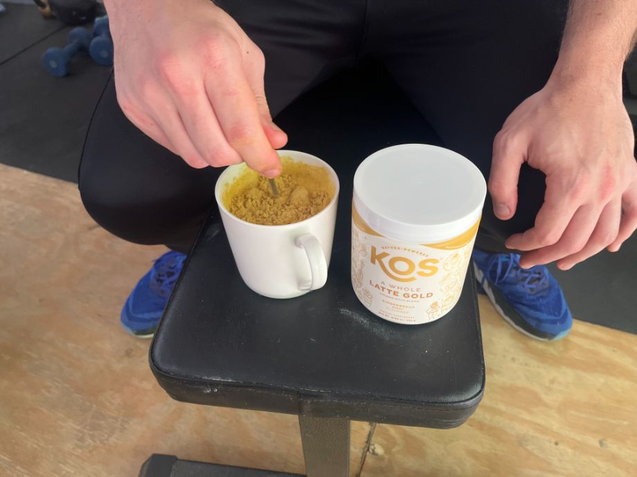 Someone stirring KOS A Whole Latte Gold turmeric powdered drink mix into a mug