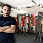 Coop of Garage Gym Reviews stands in a gym full of squat racks, benches, and weight plates.