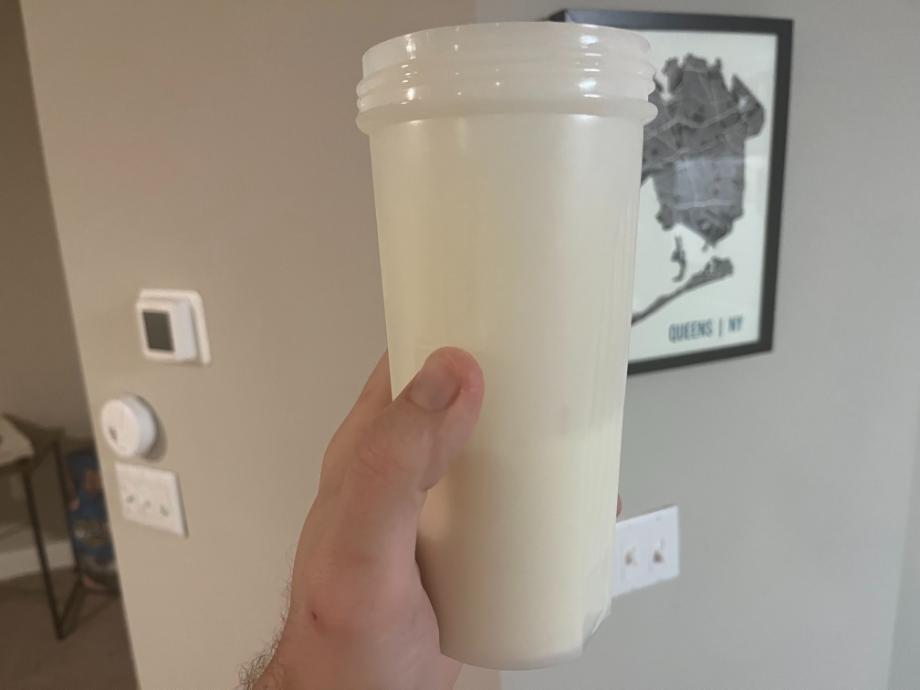 A hand holds up a white shaker cup full of Legion Casein+ Protein Powder shake