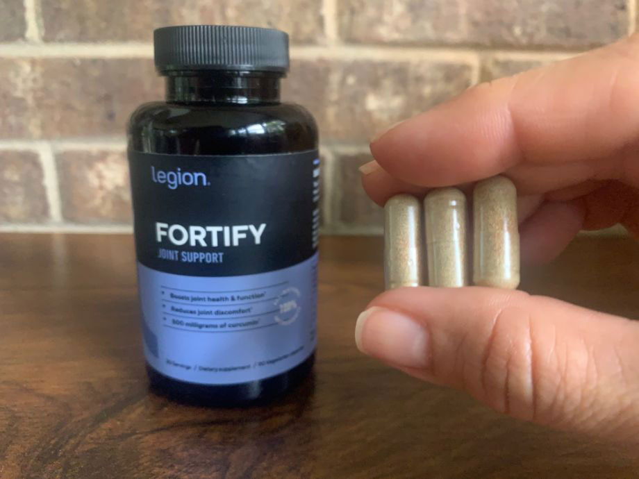 A person holds up 3 Legion Fortify capsules next to the bottle