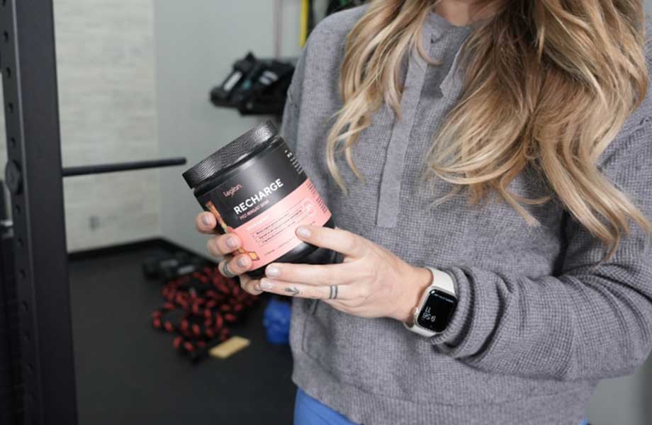 A woman holds up a container of Legion Recharge Post-Workout