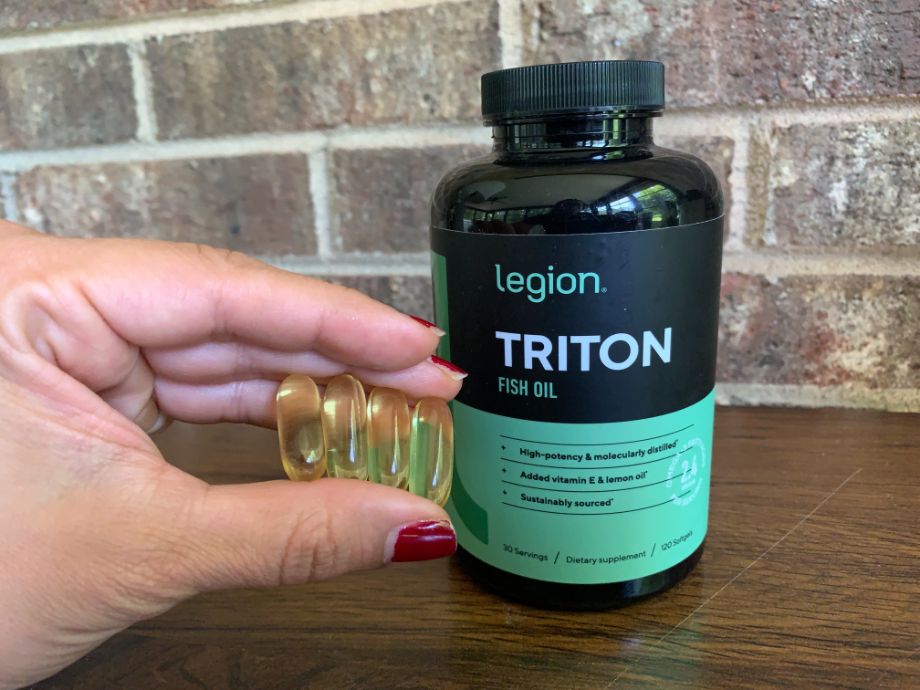 An image of a woman's hand holding Legion Triton fish oil capsules