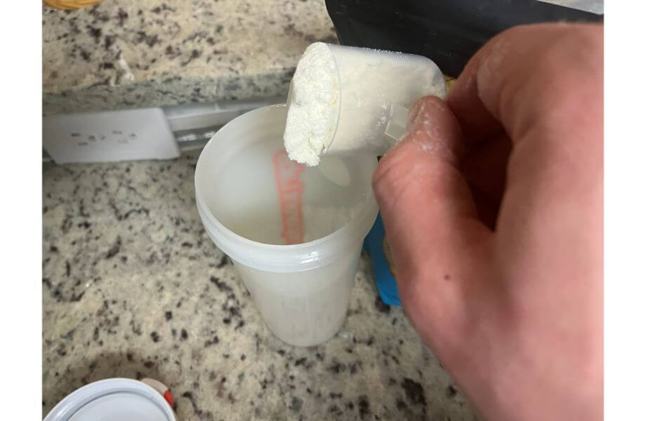 Close-up of a hand with a scoop of Legion's floury Whey Protein Powder being poured into a shaker bottle.