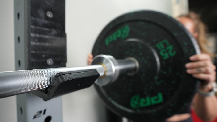 Weights are being added to one end of a Living.Fit Barbell